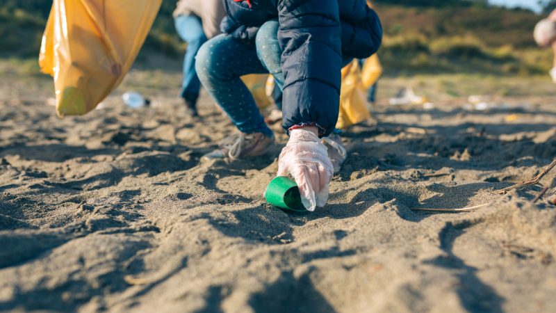 Unrecognizable little girl picking up trash with group of volunteers on the beach